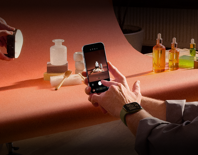 Sesión de fotos en un lugar de trabajo, una persona usa un iPhone para fotografiar productos sobre un fondo, otra sostiene una lámpara