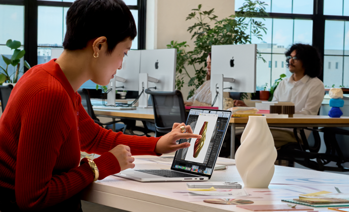 En una oficina de espacio abierto, una persona utiliza el control táctil para interactuar con el MacBook Pro con pantalla PROLED XDR