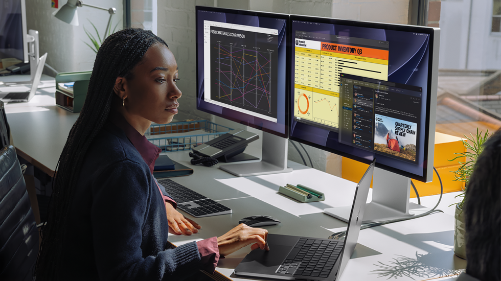 Una mujer trabaja en su mesa con un MacBook Pro conectado a dos monitores externos