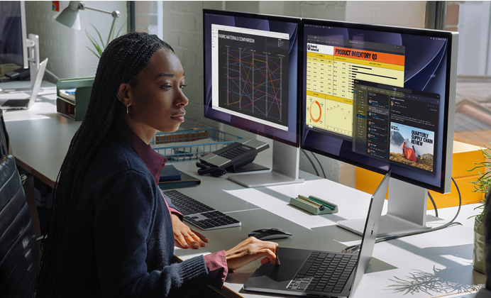 Una mujer trabaja en su mesa con un MacBook Pro conectado a dos monitores externos