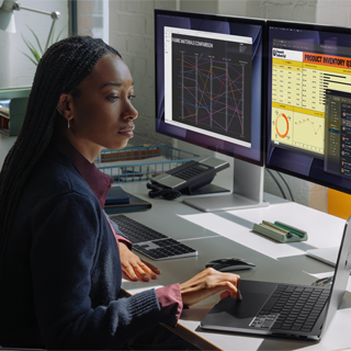 Una mujer trabaja en su mesa con un MacBook Pro conectado a dos monitores externos